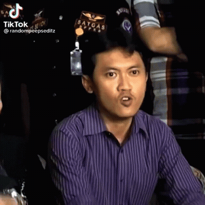 A Man In A Purple Striped Shirt Is Making A Funny Face While Sitting In A Crowd . GIF