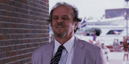 A Man In A Purple Suit And Tie Is Smiling In Front Of A Brick Wall GIF