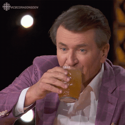 A Man In A Purple Suit Is Drinking From A Glass With #Cbcdragonsden Written On The Bottom GIF