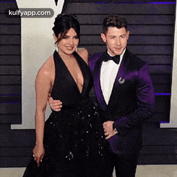 A Man In A Purple Suit Is Standing Next To A Woman In A Black Dress . GIF