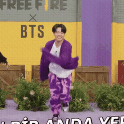 A Man In A Purple Sweater And Purple Pants Is Dancing In Front Of A Free Fire Sign GIF