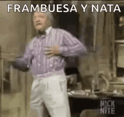 A Man In A Purple Sweater And White Pants Is Dancing In A Room With His Hands On His Chest . GIF