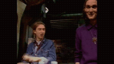 A Man In A Purple Sweater Is Waving At Another Man In A Blue Shirt . GIF