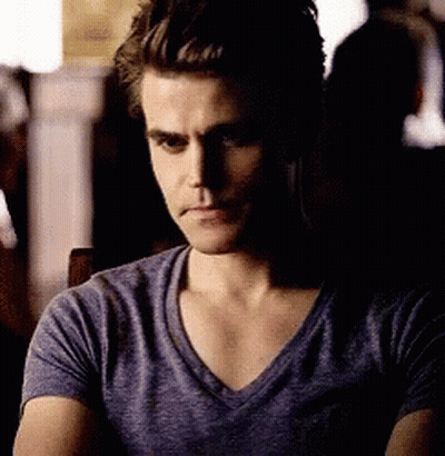 A Man In A Purple T-Shirt Is Sitting In A Dark Room . GIF