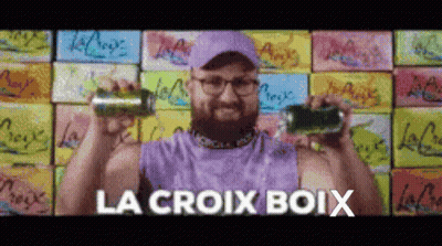 A Man In A Purple Tank Top Is Holding Two Cans Of Soda And The Words La Croix Boix Are Above Him GIF