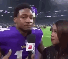 A Man In A Purple Vikings Jersey Is Being Interviewed By A Woman In Front Of A Microphone . GIF