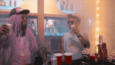 A Man In A Purple Wig Is Standing Next To A Man In A White Tank Top That Says ' Sally ' GIF