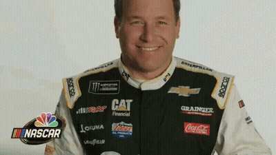 A Man In A Race Car Uniform Is Smiling With A Nascar Logo In The Background GIF