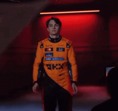 A Man In A Racing Suit Is Standing In Front Of A Red Light . GIF