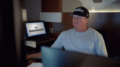 A Man In A Raiders Hat Sits In Front Of A Computer GIF