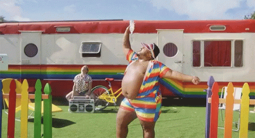 A Man In A Rainbow Outfit Stands In Front Of A Rainbow Trailer GIF