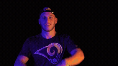 A Man In A Rams T-Shirt Is Making A Peace Sign With His Hands In Front Of His Face . GIF