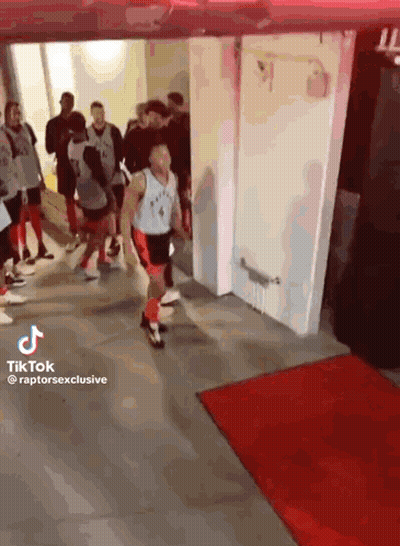 A Man In A Raptors Jersey Is Walking Through A Hallway Surrounded By People . GIF
