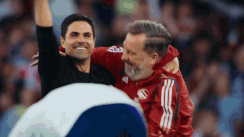 A Man In A Red Adidas Jacket Is Hugging Another Man In A Black Jacket GIF
