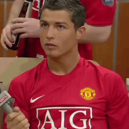 A Man In A Red Aig Jersey Is Holding A Microphone . GIF