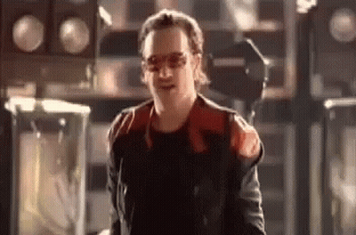 A Man In A Red And Black Jacket And Sunglasses Is Standing In A Room . GIF