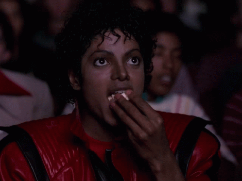 A Man In A Red And Black Jacket Is Eating Popcorn GIF