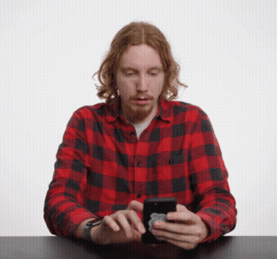 A Man In A Red And Black Plaid Shirt Is Looking At His Cell Phone GIF