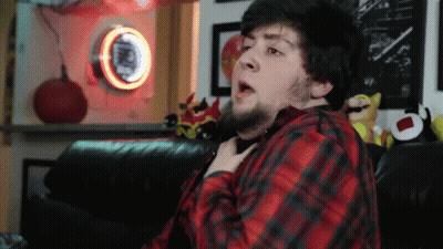 A Man In A Red And Black Plaid Shirt Is Sitting On A Couch In Front Of A Pepsi Sign GIF