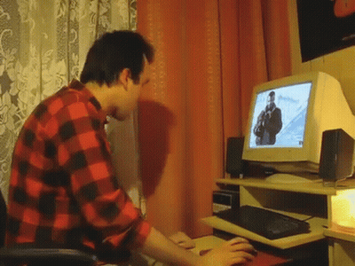 A Man In A Red And Black Plaid Shirt Is Typing On A Keyboard In Front Of A Computer Monitor . GIF