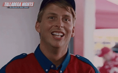 A Man In A Red And Blue Shirt Is Smiling In Front Of A Wall With Talladega Nights Written On It GIF