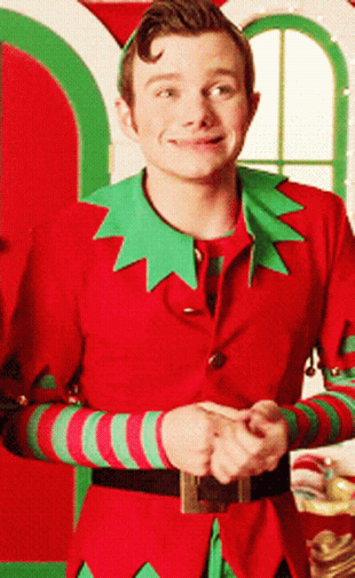 A Man In A Red And Green Elf Costume Smiles For The Camera GIF