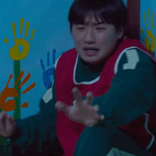 A Man In A Red And Green Vest With The Number 12 On It Is Standing In Front Of A Wall With Handprints On It . GIF