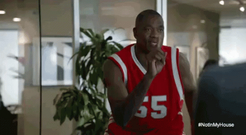 A Man In A Red And White Basketball Jersey With The Number 65 On It Is Standing In Front Of A Window . GIF
