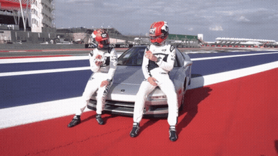 A Man In A Red And White Helmet Stands Next To Another Man In A White Suit GIF