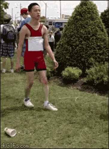 A Man In A Red And White Leotard Is Walking In The Grass GIF