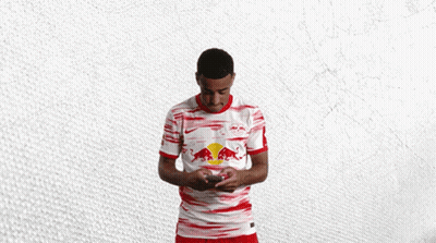 A Man In A Red And White Red Bull Shirt Holds A Cell Phone GIF
