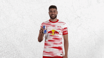 A Man In A Red And White Red Bull Shirt Holds A Red Bull Can GIF
