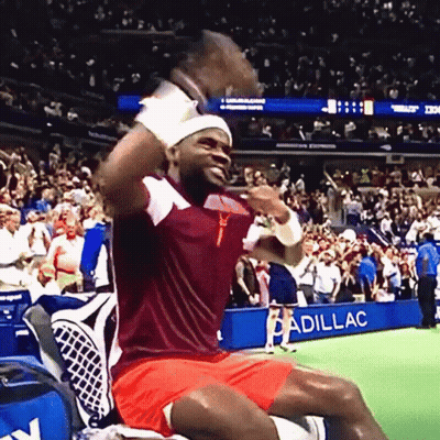 A Man In A Red And White Shirt Is Sitting In Front Of A Cadillac Sign GIF