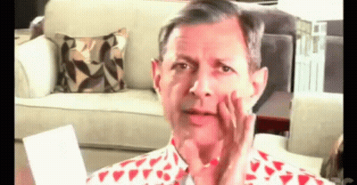 A Man In A Red And White Shirt Is Sitting In Front Of A Couch Making A Funny Face . GIF
