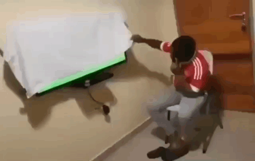 A Man In A Red And White Shirt Is Sitting In Front Of A Television With A Green Screen . GIF