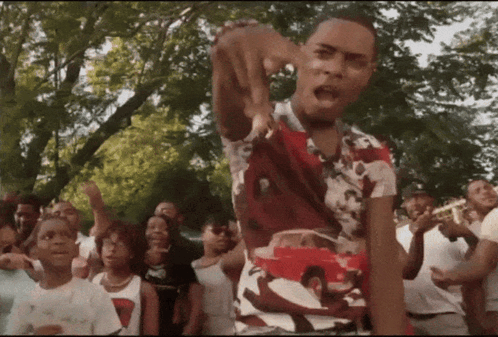 A Man In A Red And White Shirt Is Standing In Front Of A Crowd GIF