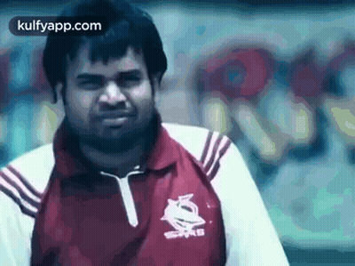 A Man In A Red And White Shirt Is Standing In Front Of A Wall With Graffiti On It . GIF
