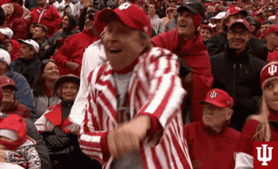 A Man In A Red And White Striped Jacket And Hat Is Dancing In A Crowd Of People . GIF