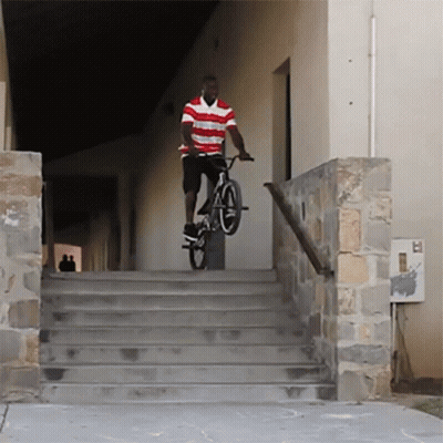 A Man In A Red And White Striped Shirt Is Riding A Bike Down Some Stairs GIF