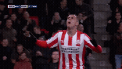 A Man In A Red And White Striped Shirt Is Standing In Front Of A Soccer Goal . GIF