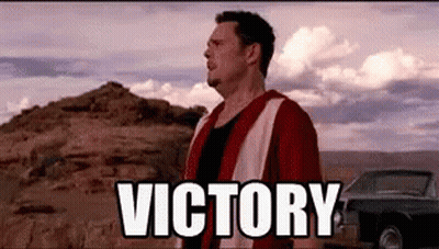 A Man In A Red And White Vest Is Standing In The Desert With The Words `` Victory '' Above Him . GIF