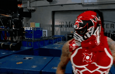 A Man In A Red And White Wrestling Outfit Stands In Front Of A T Mobile Sign GIF