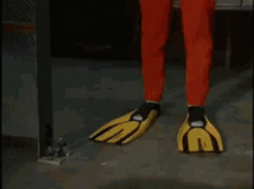 A Man In A Red And Yellow Jumpsuit And Yellow Gloves Is Standing In A Hallway . GIF