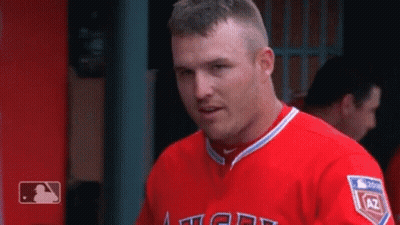 A Man In A Red Angels Jersey Is Standing In The Dugout . GIF