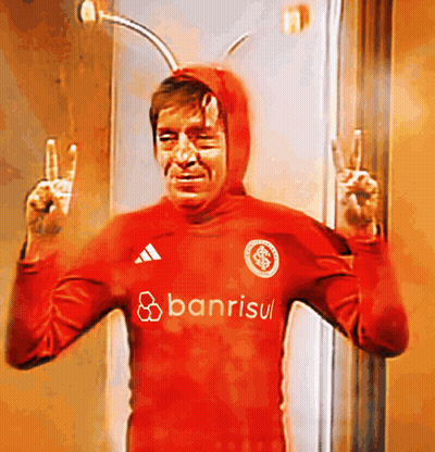 A Man In A Red Banrisul Shirt Giving The Peace Sign GIF