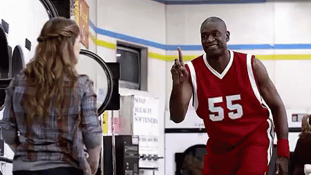 A Man In A Red Basketball Jersey With The Number 55 On It Is Pointing At A Woman In A Laundry Room . GIF