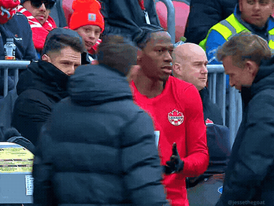 A Man In A Red Canada Shirt Stands In A Crowd Of People GIF