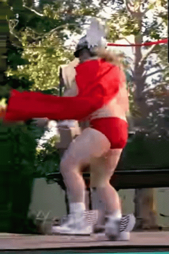 A Man In A Red Cape And Red Shorts Is Dancing On A Trampoline GIF