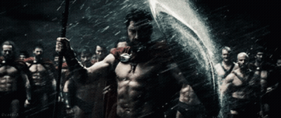 A Man In A Red Cape Is Holding A Spear And Shield In Front Of A Group Of Men GIF