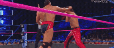 A Man In A Red Cape Is Wrestling Another Man In A Ring . GIF